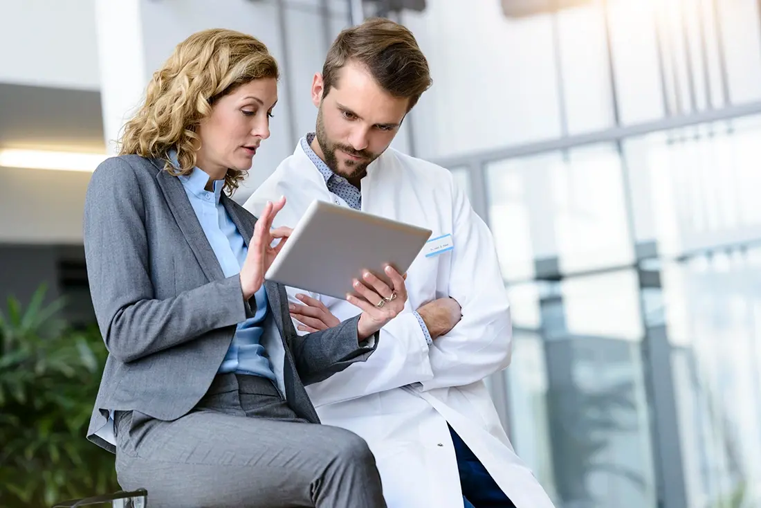 Een zakenvrouw met een tablet in haar hand in gesprek met een ziekenhuisarts