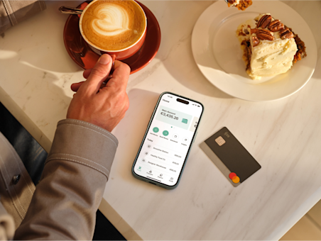 Man having a coffee and a cake and checking his bank account on his phone and his N26 card is also on the table.