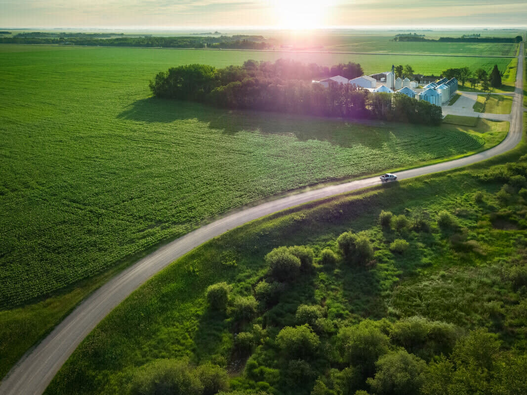 An aerial perspective of a farm and a car traveling on a country road, highlighting agricultural retail and crop planning.