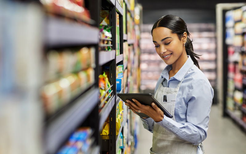 In a grocery store, a woman in an apron utilizes a tablet for trade promotion management tasks